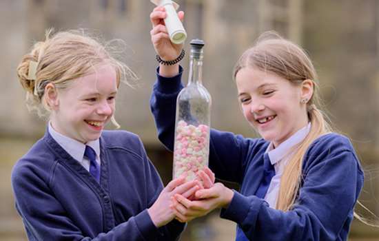 Two children in blue school uniforms hold a glass bottle filled with marshmallows at Bolsover Castle. 