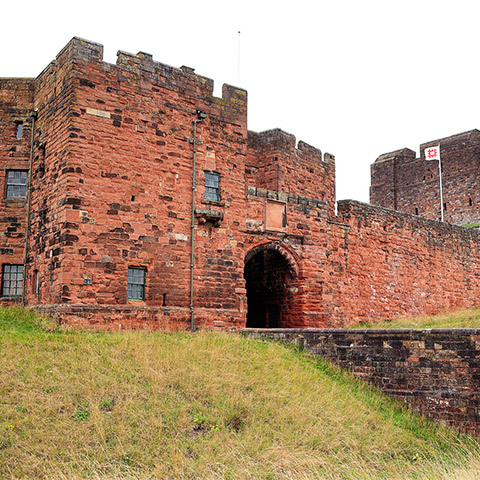 A large, red castle with a bridge leading to the front gate (Carlisle Castle)
