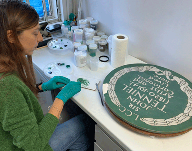 Image: a conservator works on the historic plaque to Sir John Tenniel